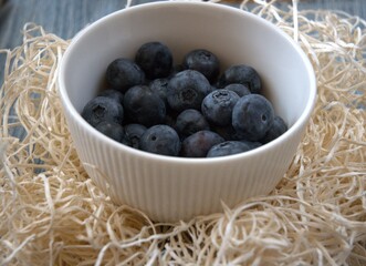 Fresh blueberries served in a white bowl decorated with straw, close-up view.