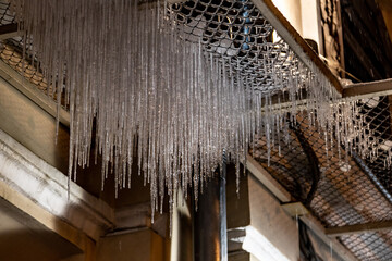 Long sharp icicles hanging from a mesh balcony in the city center. Atmospheric winter detail in...