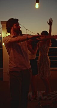 A vibrant group of diverse friends celebrates with a lively rooftop party at sunset. They dance freely, laugh, and enjoy each other's company, creating unforgettable memories under string lights.