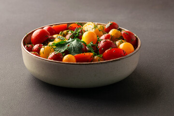 Bright juicy salad with colorful cherry tomatoes and aromatic herbs on black stone table top view. Healthy vegan food concept.

