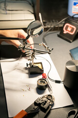 A close-up of an electronic workstation with a magnifying glass, soldering tools, and cables being prepared for repair