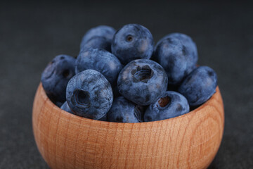 Fresh ripe blueberries in small wooden bowl on dark gray textured stone background. Delicious organic fruit rich in vitamins, wild berries,healthy lifestyle, natural food. Close up, macro