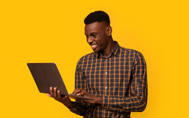 Freelance Work. Portrait Of Smiling African American Guy Using Laptop While Standing Isolated Over Yellow Background, Black Millennial Guy Working Online, Enjoying Remote Job Opportunities, Copy Space