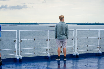 Man standing on ferry deck looking at sea.