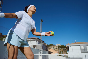 Young Woman Focused on Tennis Serve on Outdoor Court under Sunny Skies