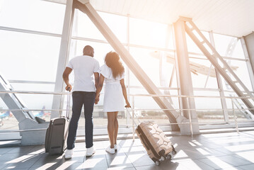 Summer vacation. Loving african newlyweds looking at window, waiting for departure at airport, back view, empty space