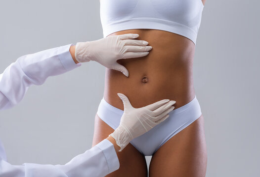 Cropped of plastic surgeon hands checking afro woman belly before beauty procedure, liposuction concept