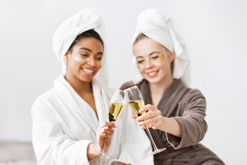 Relaxed girlfriends with eye patches on toasting with champagne while having skincare procedures at home © Prostock-studio