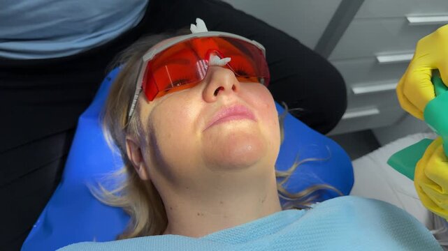 Dentist's hands in gloves with dental punch and cofferdam scarf. Dentist treats woman's tooth to patient with rubber dam. Modern dental office. Treatment elimination of caries, installation of filling