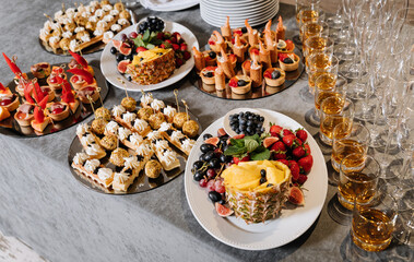 Elegant catering table with assorted canapes, fresh fruits and whiskey glasses