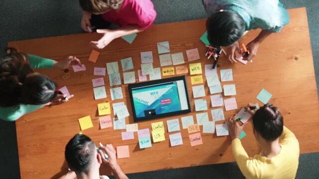 Top down view of programmer brainstorming and planning about web design while looking at tablet wireframe prototype. Aerial view of skilled developer team talking about digital application. Symposium.