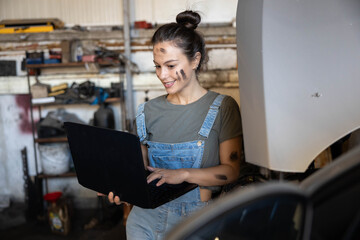 A focused woman with dirt on her face uses a laptop in a garage, symbolizing modern work and casual creativity.