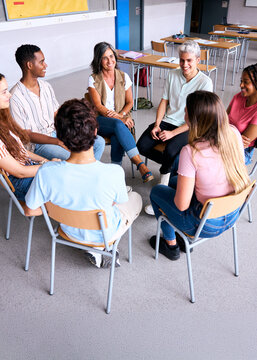 Vertical. A group of students and a teacher sit in a circle during a school group therapy session, promoting communication, trust and mental health support among teenagers.