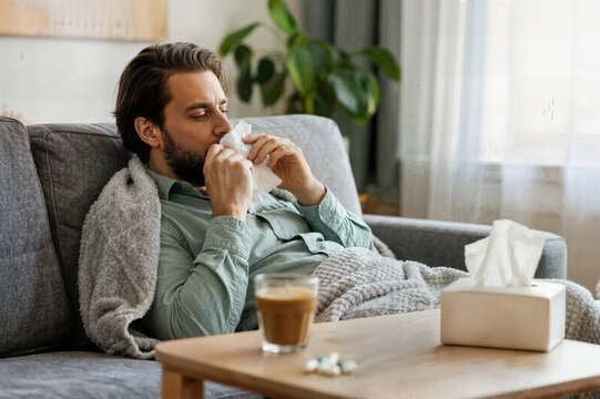 ill young man sneezing concept lemon tea on table at home joven enfermo estornudando con té de limón sobre la mesa en casa jeune homme malade éternuant avec une tasse de thé au citron sur la table