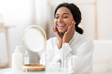 Self-Care Concept. Beautiful Black Woman Looking At Magnifying Mirror And Touching Face, Attractive African American Female Wearing White Silk Robe Making Beauty Treatments At Home, Free Space