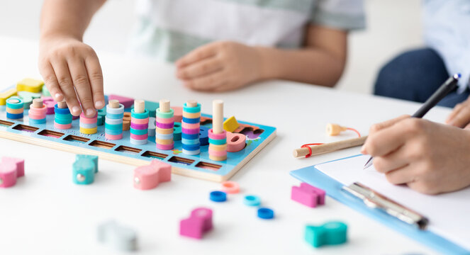 Modern organic toys for kids. Close up shot of unrecognizable little boy playing developing wooden game at psychologist office, specialist taking notes