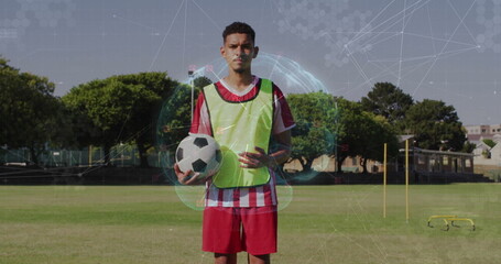 Standing soccer player holding ball wearing neon pinnie near agility poles on training field
