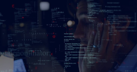 Mid-adult man focusing on code on monitor in home office, with laptop keyboard glasses reflection