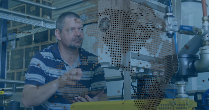 Standing male technician gesturing towards machinery in factory, with tablet and world map overlay