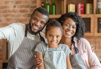 Obraz premium Happy african family taking selfie at kitchen, wearing aprons and smiling at camera
