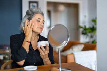Senior woman applying moisturizing cream on face at home