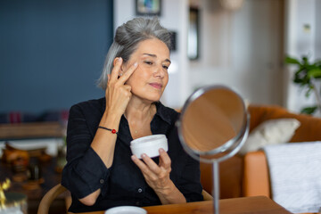 Senior woman applying face cream at home