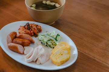 Japanese breakfast plate with sausage, chicken ham, omelet, salad, and soup
