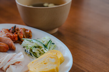 Japanese breakfast plate with sausage, chicken ham, omelet, salad, and soup
