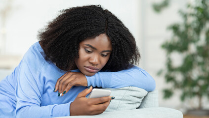 Depression Concept. Portrait of frustrated african american woman looking at smartphone, checking...