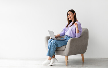 Millennial Caucasian woman having creative idea, gesturing eureka, sitting in armchair with laptop...