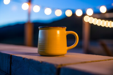 Cozy themed stock photo A yellow coffee mug against blurred string lights, evoking feelings of relaxation and evening ambiance