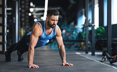 Push ups workout. Muscular athlete training on floor at gym, empty space