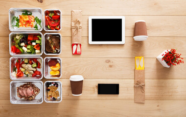 Online healthy restaurant food order, diet plan. Fresh daily meals delivery. Fitness nutrition, vegetable, meat and fruits in foil boxes, coffee and tablet. Top view, flat lay on wood with copy space