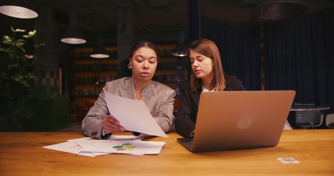 Women compare data in report and enter information into laptop