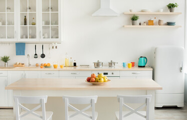 Healthy food, vitamins, interior and design of modern apartment. Colored apples on plate on table, teapot and bright cups on white furniture and dining room with dishes in morning, empty space