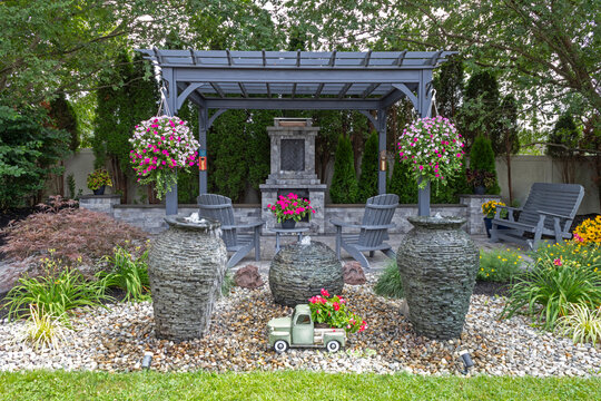 Wooden gray pergola on pavers with stone fireplace and waterfall urns landscape design idea for backyard sanctuary