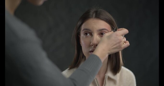 A makeup artist applies foundation to a model's face using a makeup sponge in a professional setting.