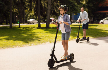 Time With Family. Laughing son using motorized kick scooter with his dad on a sunny day, copy space