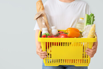 Woman holding yellow shopping basket with different fresh products on grey background
