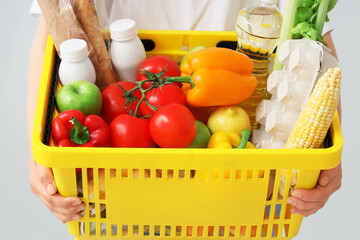 Woman holding yellow shopping basket with different fresh products on grey background