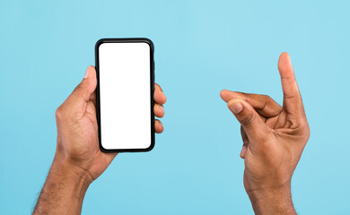 Cropped view of young black guy showing smartphone with empty white screen and holding something on blue background, mockup for mobile app, website and business card design