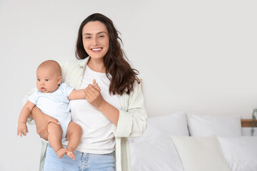Beautiful young happy mother with her cute little baby in bedroom at home