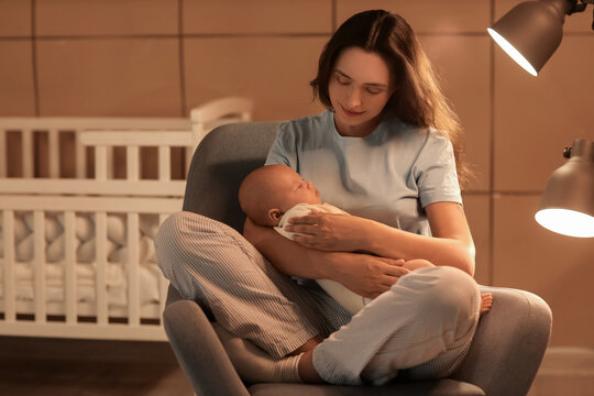 Happy young mother with her cute little sleeping baby sitting on armchair in bedroom at night - Powered by Adobe