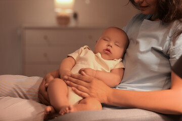 Happy young mother with her cute little sleeping baby sitting on armchair in bedroom at night, closeup