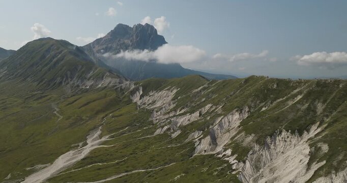 Aerial view of the majestic Gran Sasso mountains with sharp ridges and green grass contrasting with white rocky pathways, Gran Sasso, Abruzzo, Italy.