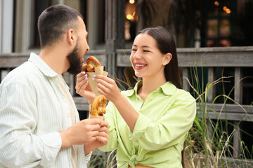 Young happy couple with tasty pretzels walking along city street