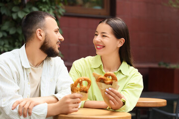 Young happy couple with tasty pretzels sitting in cafe