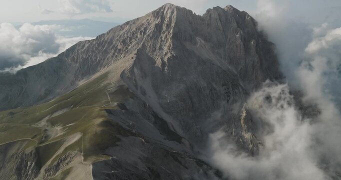Aerial view of the majestic Gran Sasso mountains piercing through the clouds with rocky terrain and sparse vegetation, Gran Sasso, Abruzzo, Italy.