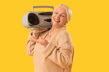 Senior woman with boombox on yellow background