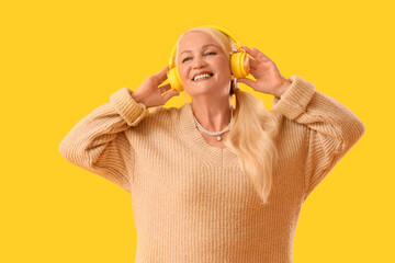 Senior woman in headphones listening to radio on yellow background